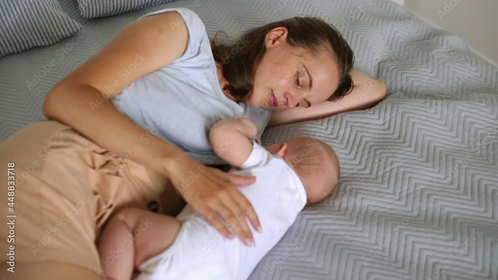 Side view of mom lying with a baby in a bed on gray blanket feeding breast milk, breastfeeding, lactation, maternal love, caring for a newborn, a happy family.