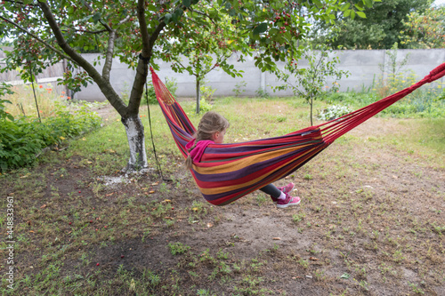 Little girl with pigtail swinging in striped hammock in the garden