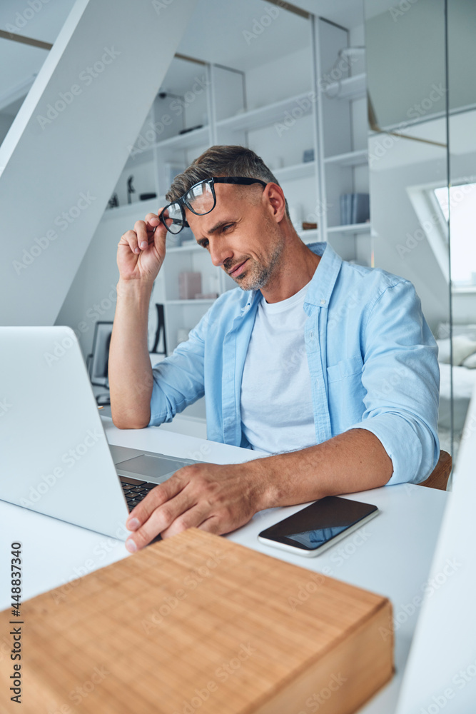 Fototapeta premium Tired mature man working on laptop while sitting at the office desk