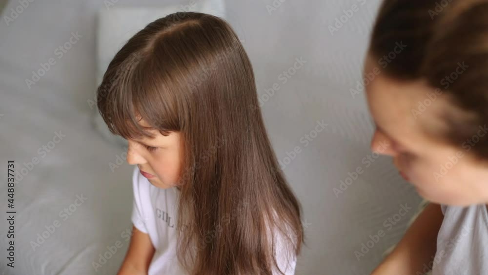 Cute dark haired girl sitting on sofa and crying while mother combing her hair, sad preschooler kid making hairstyle, haircare, preparing for going to kindergarten. Cute dark haired girl sitting on sofa and crying while mother combing her hair, sad preschooler kid making hairstyle, haircare, preparing for going to kindergarten.