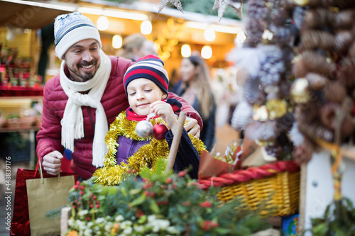 Happy man with small daughter buying decorations for Xmas in Christmas market. Focus on girl