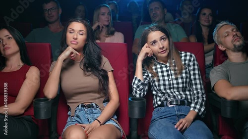 Two upset woman friends watching bad film with unpleasant negative emotion bored at cinema
