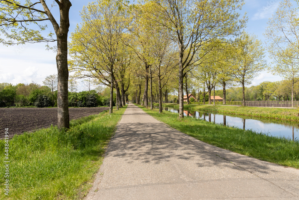 Dutch countryside in a rural area in Grientsveen with walking path, a river with reflections in the water surrounded by trees, greenery and houses on a sunny day during spring in The Netherlands