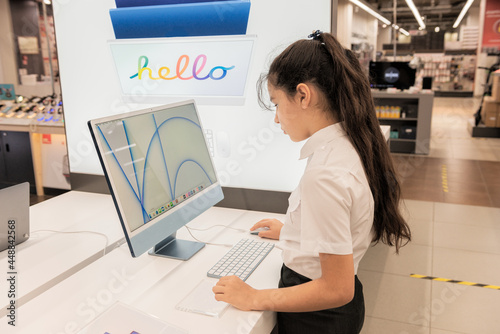 A schoolgirl girl chooses, checks and tests a computer in a store