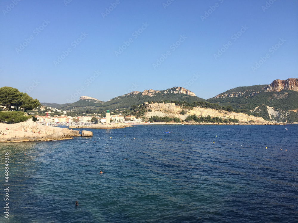 The Cassis lighthouse and harbour entrance with Château de Cassis and Cap Canaille headland in the background on a summer sunny day. Located in the Provence-Alpes-Côte d'Azur region, French Riviera.