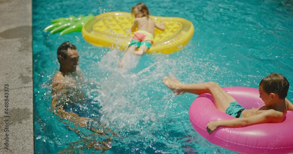 Family playing and splashing in the pool on summer vacation, cinematic family lifestyle