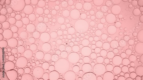Big clear bubble moves along pale pink smaller ones moving them and explodes on pale pink background | Macro shot of moisturizer with glycerin for its commercial photo