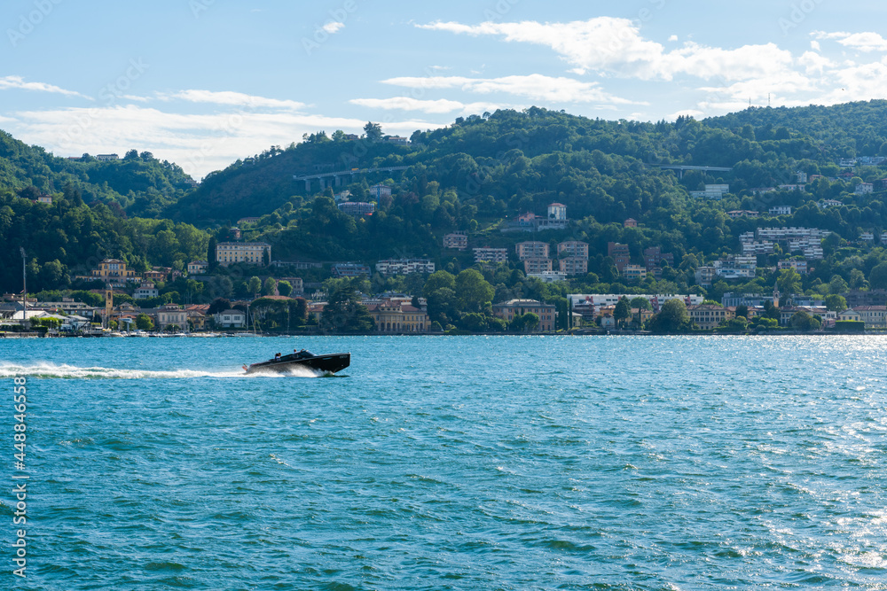 Fast speedboat sailing over the Como lake, in the bay of Como city. It is a beautiful sunny summer day.