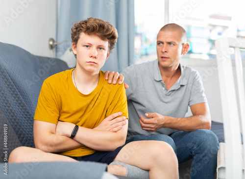 Portrait of father calming upset teenage son after quarrel