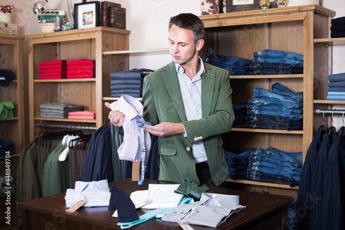 Positive male seller displaying diverse cloths in clothes shop