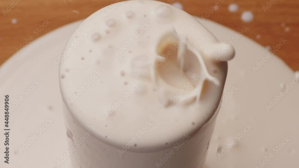 Yoghurt pouring into a glass and brim over the edgeon table, close up Yoghurt pouring into a glass and brim over the edgeon table, close up
