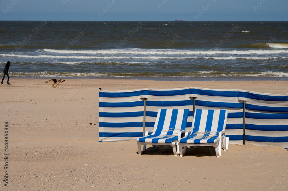 Blue-white sun beds on yellow sandy beach in small Belgian town De Haan or Le Coq sur mer, luxury vacation destination, summer holidays Blue-white sun beds on yellow sandy beach in small Belgian town De Haan or Le Coq sur mer, luxury vacation destination, summer holidays