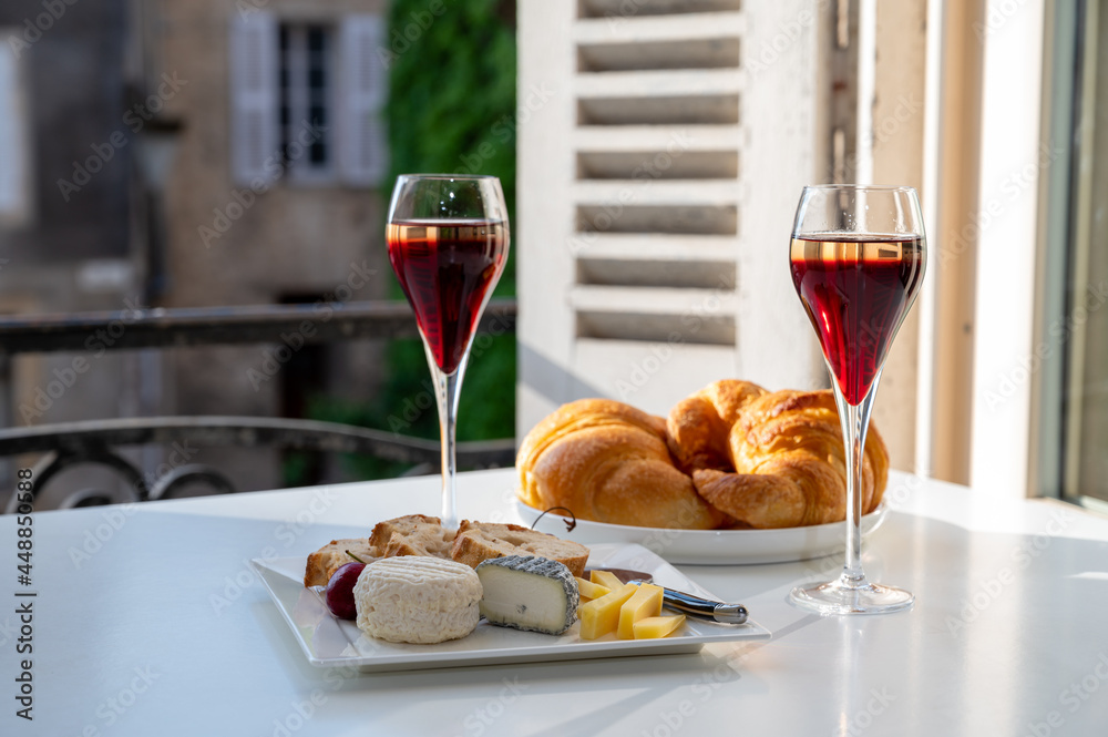 Drinking of Kir Royal, French aperitif cocktail made from creme de cassis topped with champagne, typically served in flute glass, with view on old French village Drinking of Kir Royal, French aperitif cocktail made from creme de cassis topped with champagne, typically served in flute glass, with view on old French village