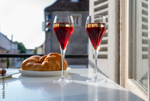 Drinking of Kir Royal,  French aperitif cocktail made  from creme de cassis topped with champagne, typically served in flute glass, with view on old French village