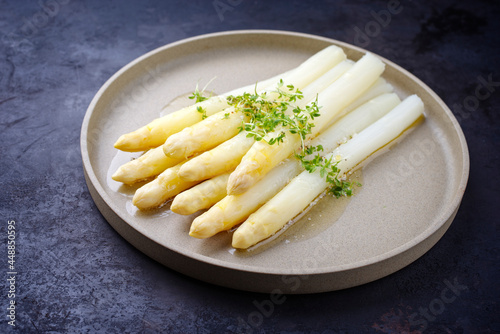 Modern style traditional steamed white asparagus with butter sauce hollandaise and cress served as close-up on a Nordic design plate