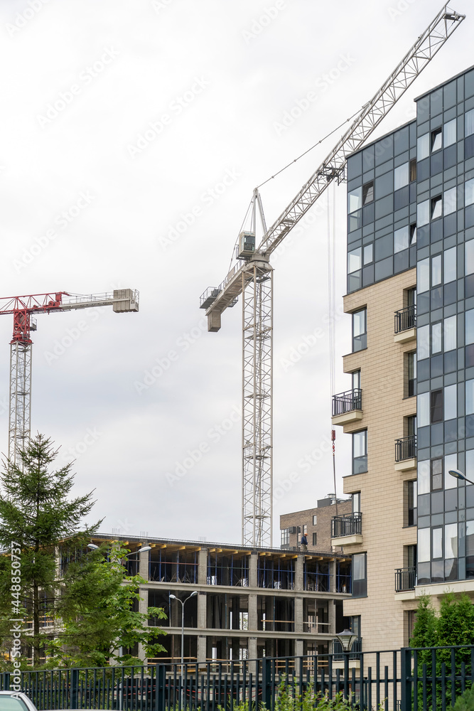 Finished residential building, unfinished residential buildings and construction cranes against clear blue sky. Housing construction site, apartment block with scaffolding