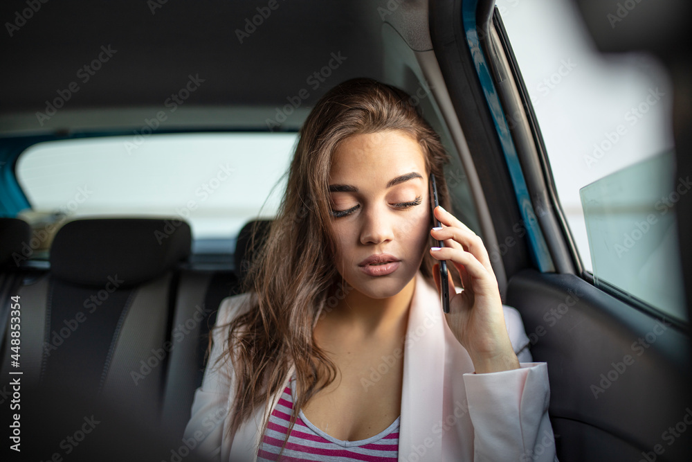 Sad young woman looking through the car window. Bored woman in a car. Pensive woman looking out of a car window. Sad young woman in the car talking with smartphone