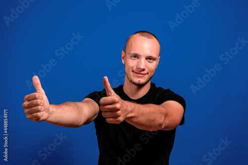 Young caucasian man with blue eyes raising his thumbs up in approval isolated on blue studio background. Approval concept