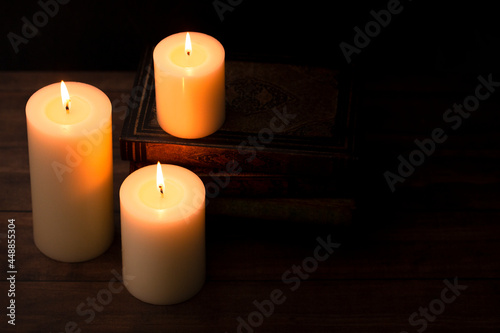 Three Pillar Candles Burning in a Dark Room with a Stack of Antique Books © pamela_d_mcadams