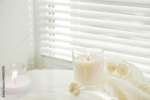 Burning candles and white sweaters on the windowsill. Cozy autumn concept and a window with blinds...