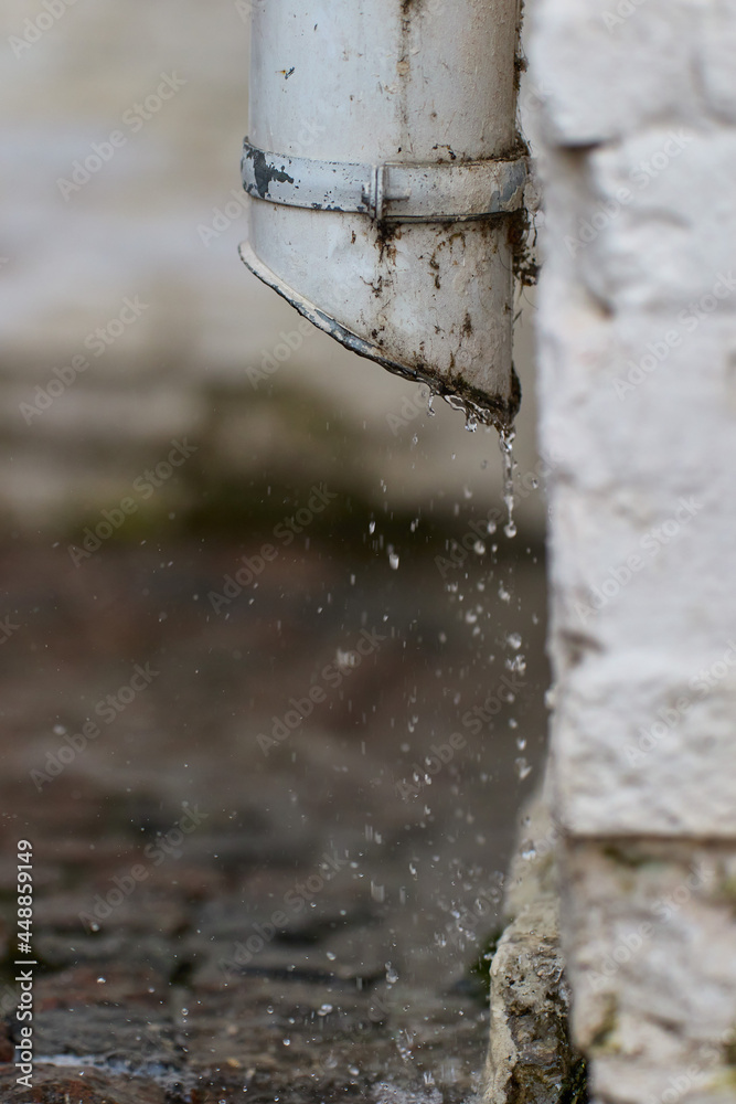 The water falls from the gutter onto the sidewalk The water falls from the gutter onto the sidewalk