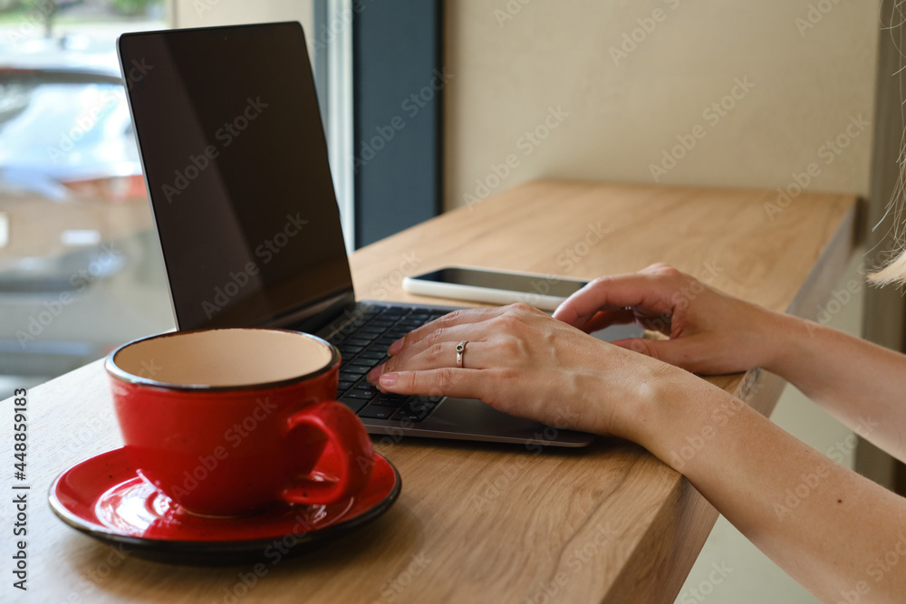 The girl sits at the table and works at a laptop and a smartphone. Remote work from home, cafe, business space. Business lady at work. Business background. Home office The girl sits at the table and works at a laptop and a smartphone. Remote work from home, cafe, business space. Business lady at work. Business background. Home office