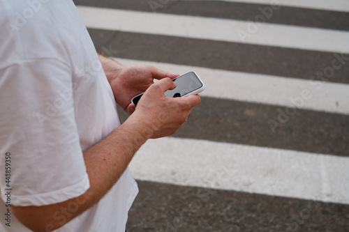 Man looks at a smartphone while crossing the road.
The pedestrian does not follow the road rules. A man stands at an intersection with a phone in his hands and looks at the screen. Smartphone close-up