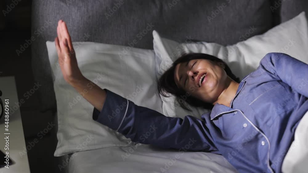 Middle aged woman in blue pajamas full of energy stretching and yawning in bed during sunny morning. Awakening concept. Middle aged woman in blue pajamas full of energy stretching and yawning in bed during sunny morning. Awakening concept.