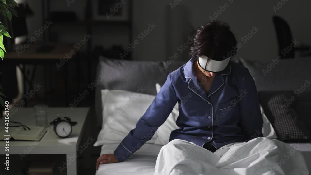 Middle aged woman in sleep mask and pajamas unable to wake up in bed. Early morning awakening. Exhaustion and no energy concept. Middle aged woman in sleep mask and pajamas unable to wake up in bed. Early morning awakening. Exhaustion and no energy concept.