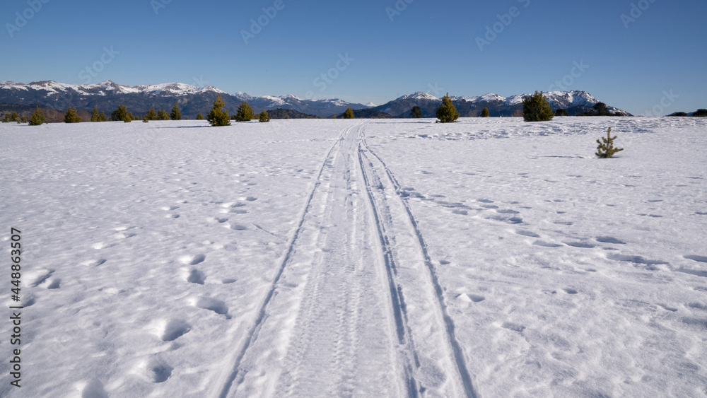 Alpine winter landscape. View of the truck tracks across the white field covered with snow in the mountains in a sunny day.