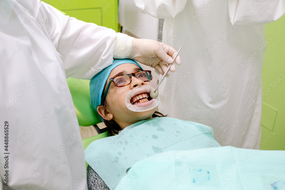 Crop dentist examining teeth of boy near assistant Crop dentist examining teeth of boy near assistant