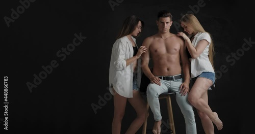 Handsome man and two beautiful women on dark background. Polyamory concept photo