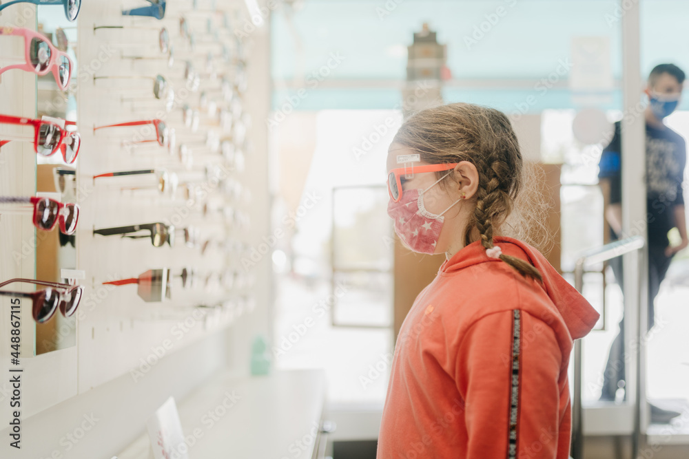 Young girl wearing a face mask trying out glasses Young girl wearing a face mask trying out glasses