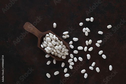 White kidney beans in wooden scoop isolated on wooden background close up. Top view.