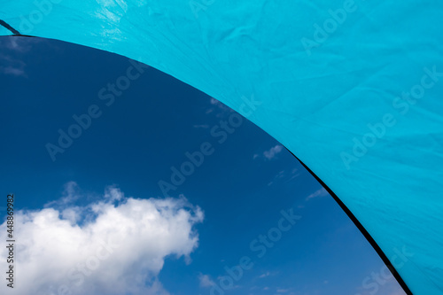 Blue sky and withe clouds seen from inside a blue tent. Picture taken in good lighting conditions  in the middle of a sunny day