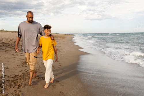 Father and son walking embracing on the beach photo