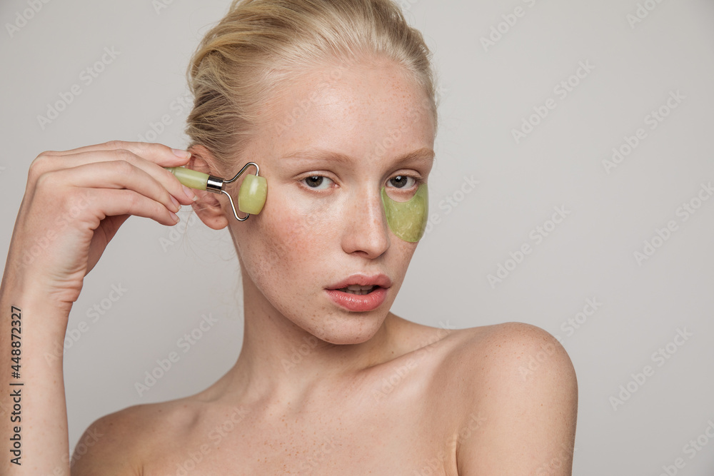 © Anna Tabakova/Stocksy - Model with green jade roller and under-eye patch © Anna Tabakova/Stocksy - Model with green jade roller and under-eye patch