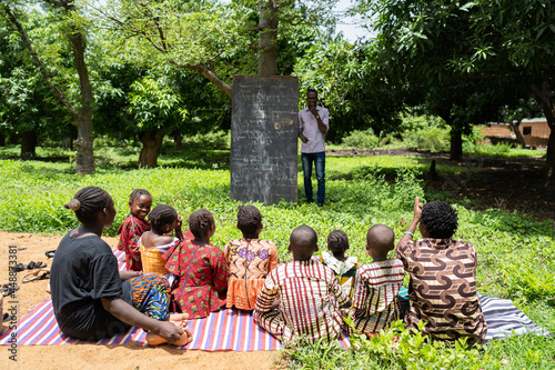 Group of children in an open air class listening to their teacher in a poor african village school