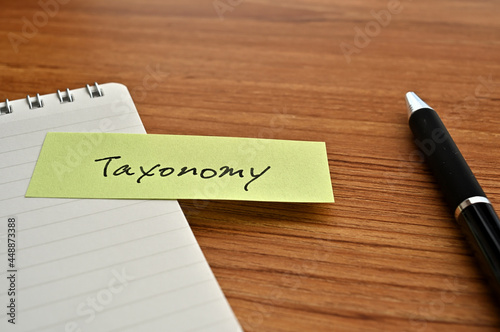 There is sticky note with the word of Taxonomy on the desk with a pen. © hogehoge511