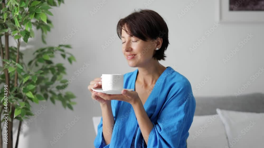 Attractive woman holding white ceramic cup and taking smell of fresh aromatic coffee. Caucasian dark haired lady enjoying morning beverage at home. Attractive woman holding white ceramic cup and taking smell of fresh aromatic coffee. Caucasian dark haired lady enjoying morning beverage at home.