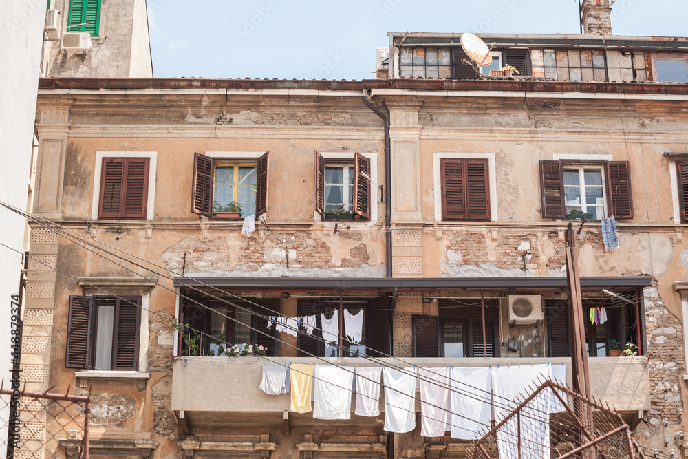 Typical italian mediterranean facade of a residential building, old and decaying with traditional laundry drying on windows and a balcony, on a vintage house, in istria region, by the adriatic...