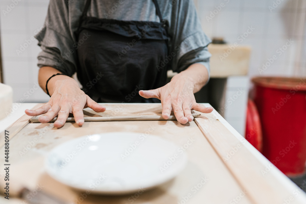 Crop artisan rolling clay in workshop