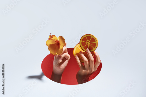 Hands through torn hole of paper with slice of orange and flower in hand
