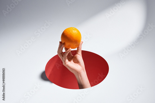 Woman's hand holding orange fruit on index finger through a hole cut in blue paper background photo