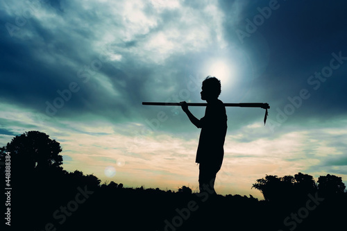 Silhouette of a farmer standing with a spade outdoors in light.