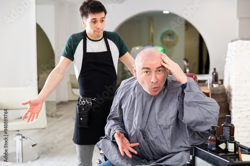 Фотография Dissatisfied man with shaved head shocked by haircut regretting hairdresser in m