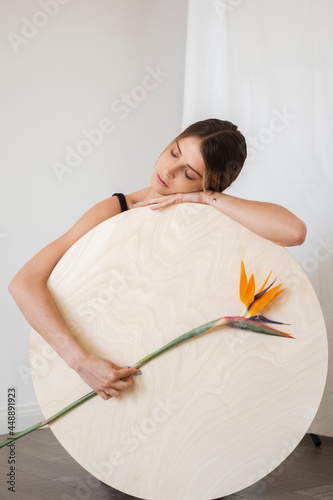 Portrait Of A Young Woman Leaning On A Wood Circular Shape Holding A Flower photo