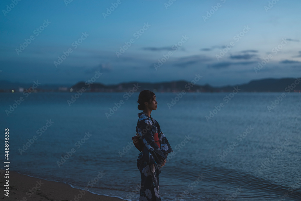 夕暮れの海にいる浴衣の女性