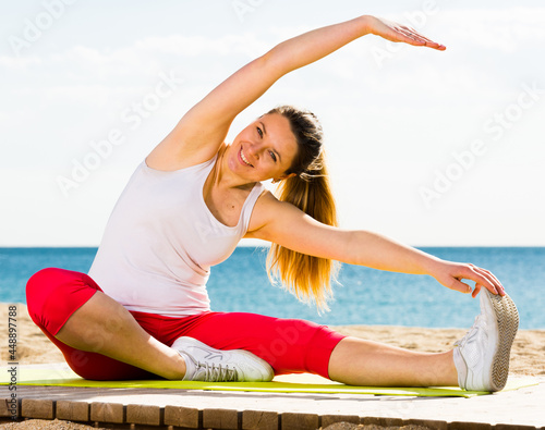 Young woman doing yoga poses sitting on sunny beach by ocean in morning