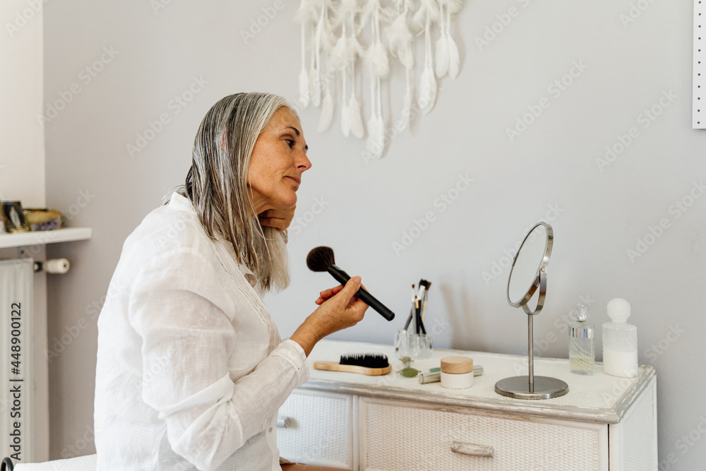 Mature woman applying makeup in bedroom Mature woman applying makeup in bedroom